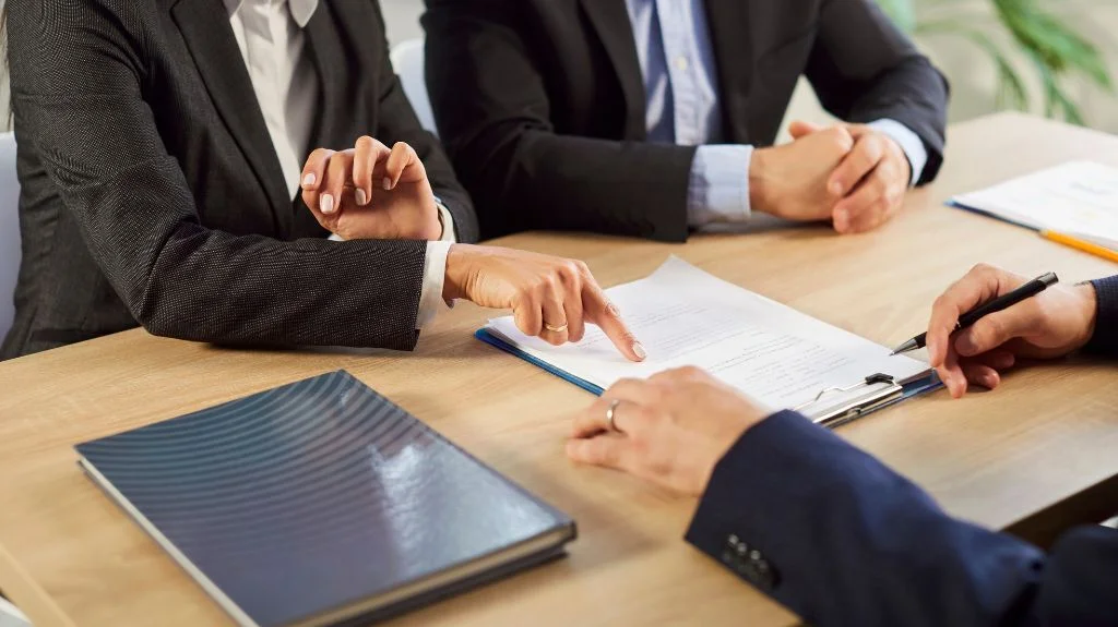 Three business professionals in suits reviewing and discussing a document on a clipboard.
