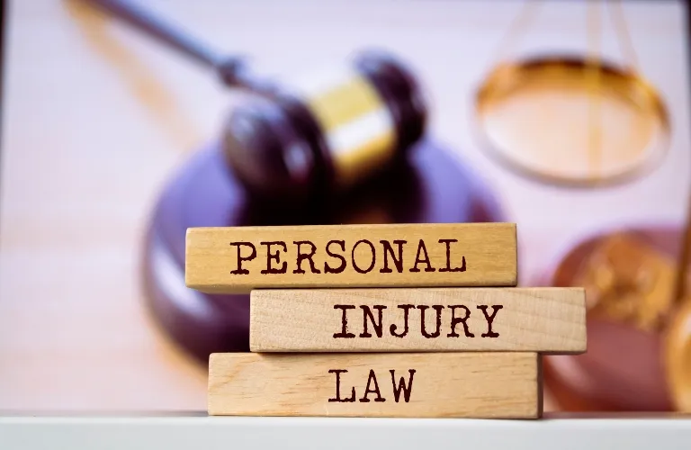 Stacked wooden blocks with the words "Personal Injury Law" in front of a blurred judge's gavel and scales.