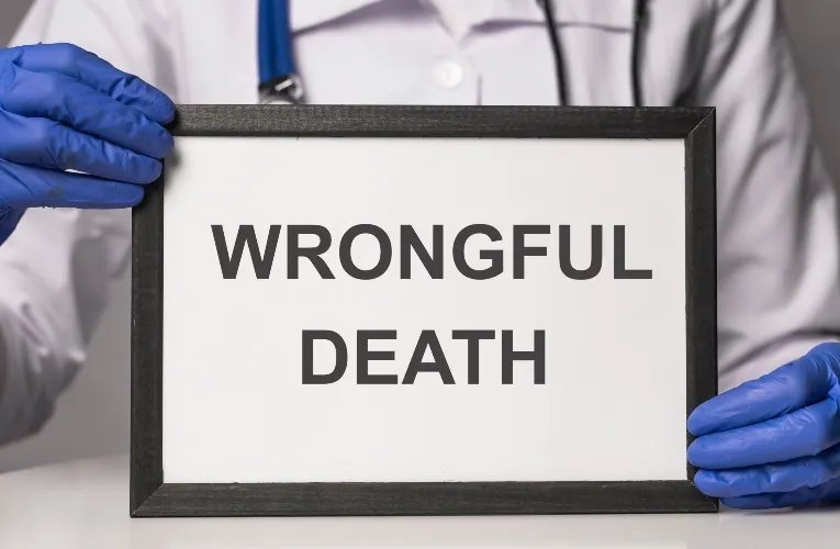 Person wearing blue gloves and white coat holding framed sign with text "WRONGFUL DEATH" in black letters.