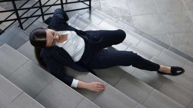 Woman in navy pinstripe suit and glasses sitting on gray stairs indoors.
