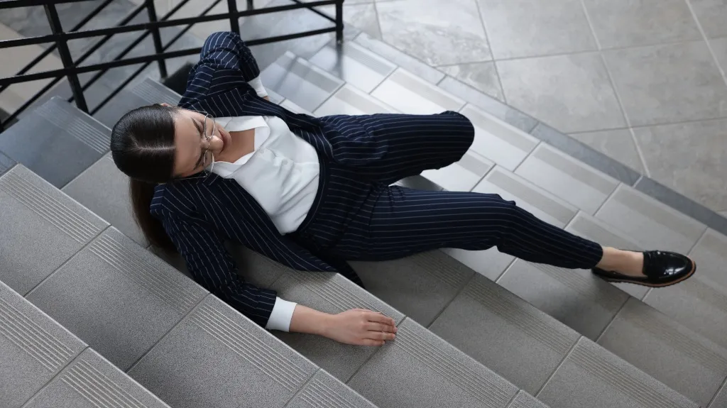 Woman in navy pinstripe suit and glasses sitting on gray stairs indoors.