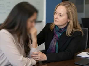 Two women in a professional setting, one offering comfort to the other.