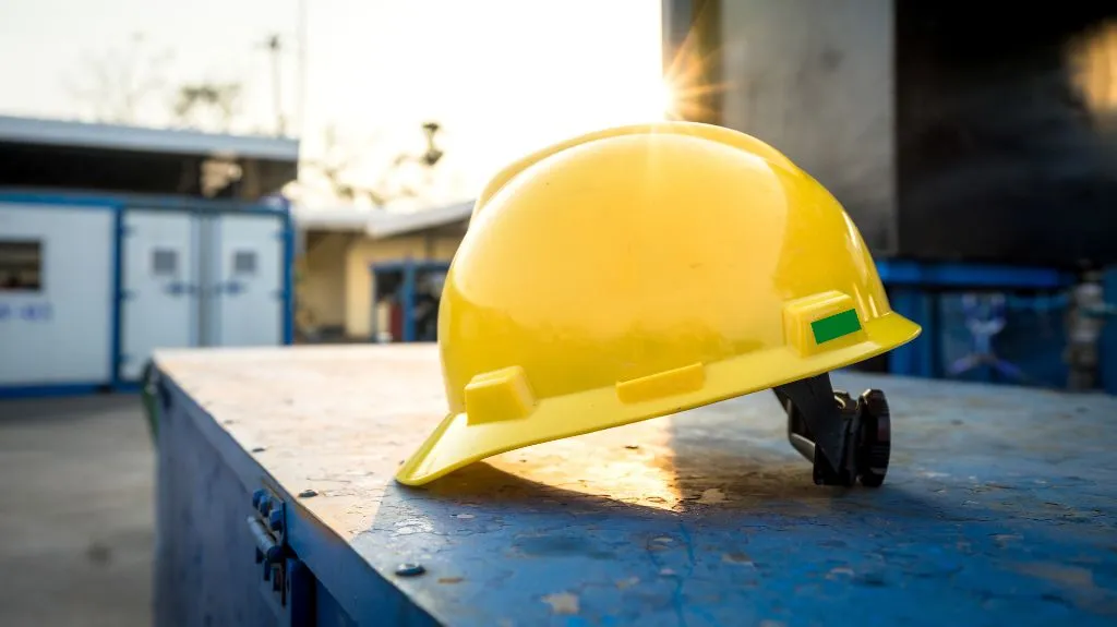 Yellow construction hard hat resting on a blue metal surface at a worksite during sunset.