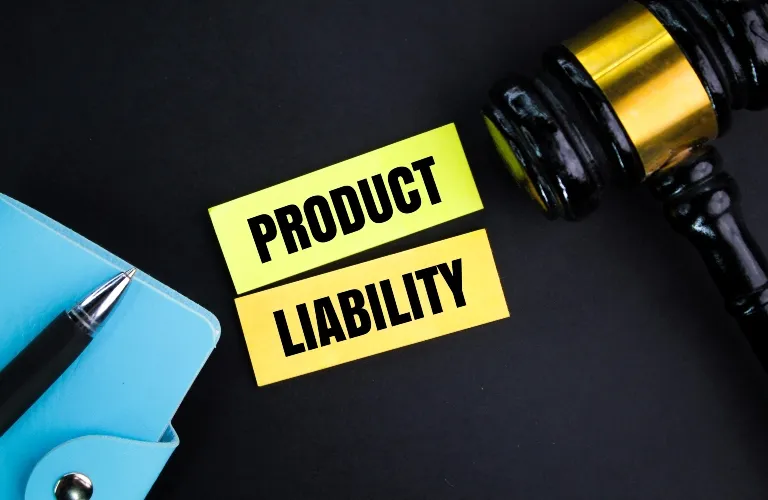 Yellow cards with the words "Product Liability," a black judge's gavel, and a blue notebook with a pen.